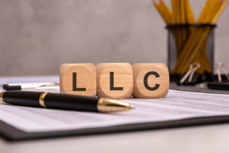 wooden cubes displaying the abbreviation LLC on a work desk with financial documents, a pen, and office supplies